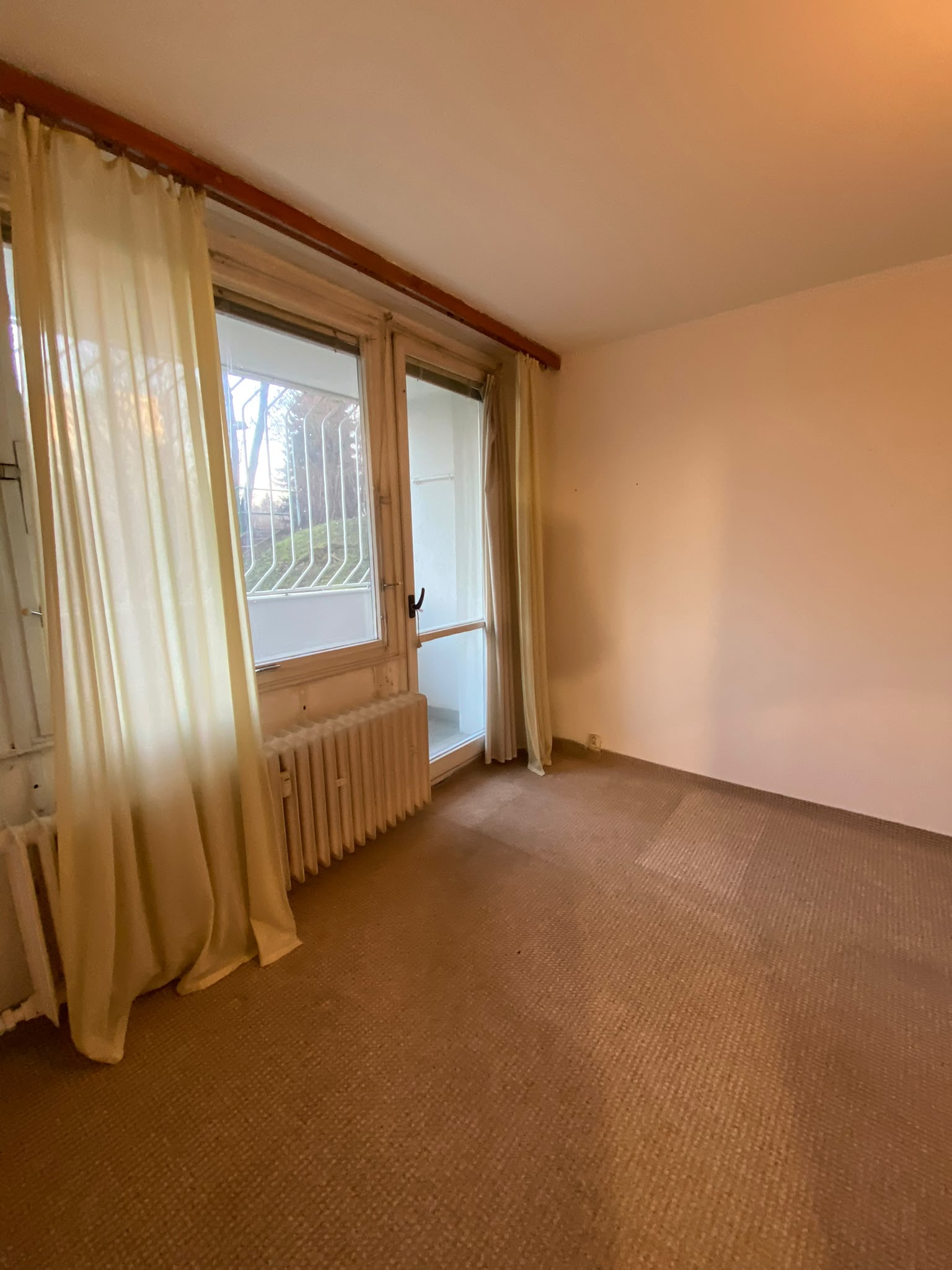 Pokoj s balkonovými dveřmi a kobercem před rekonstrukcí bytu 32 m²